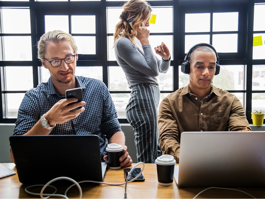 White label agency partner benefits — team of three professionals working on laptops and mobile while coordinating tasks and communication