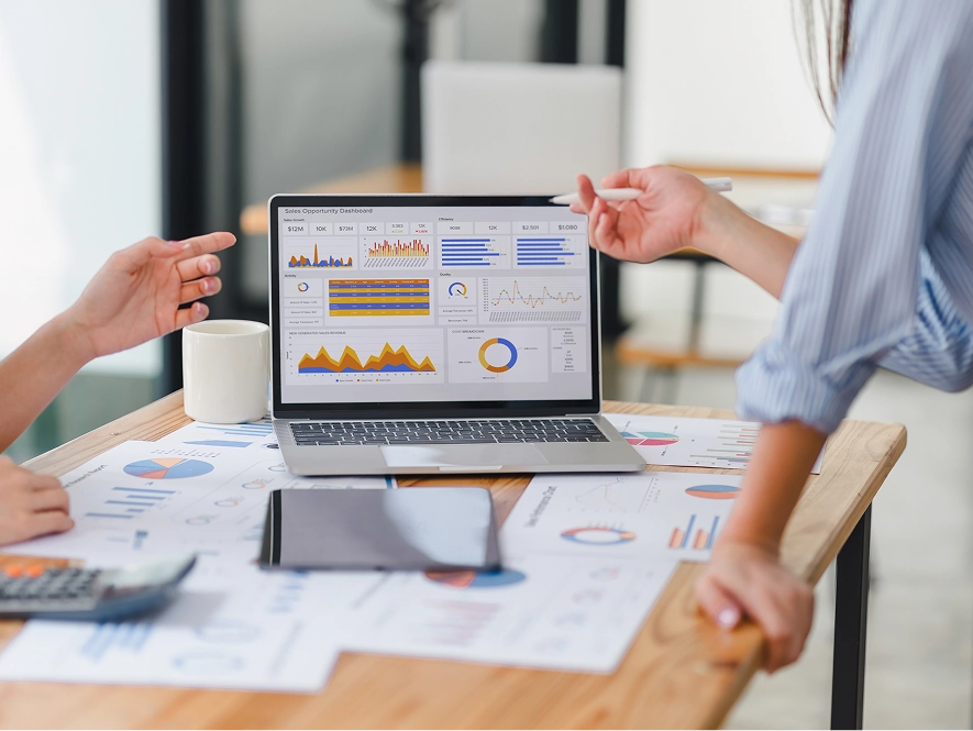 White label reporting, compliance and support — laptop on table with analytics graph on screen and charts drawn on paper nearby