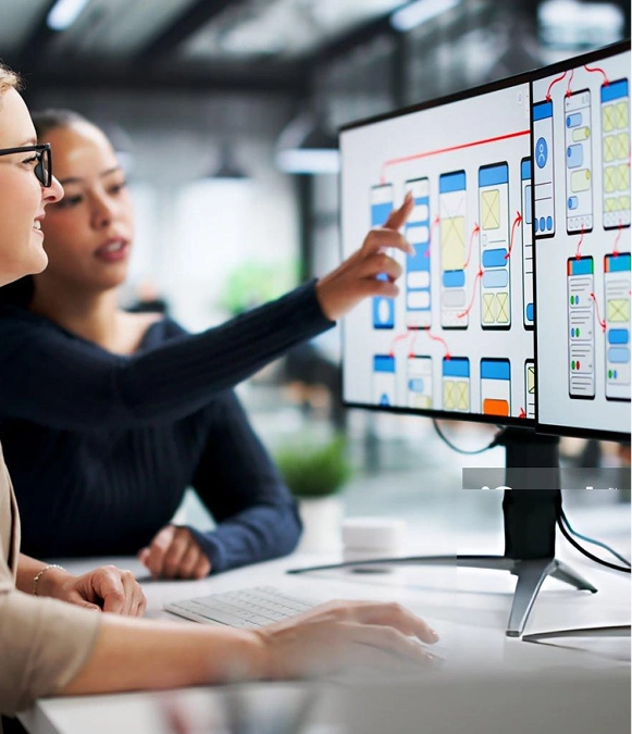 White label UI/UX design — two professionals discussing over a laptop with multiple design prototypes on desktop